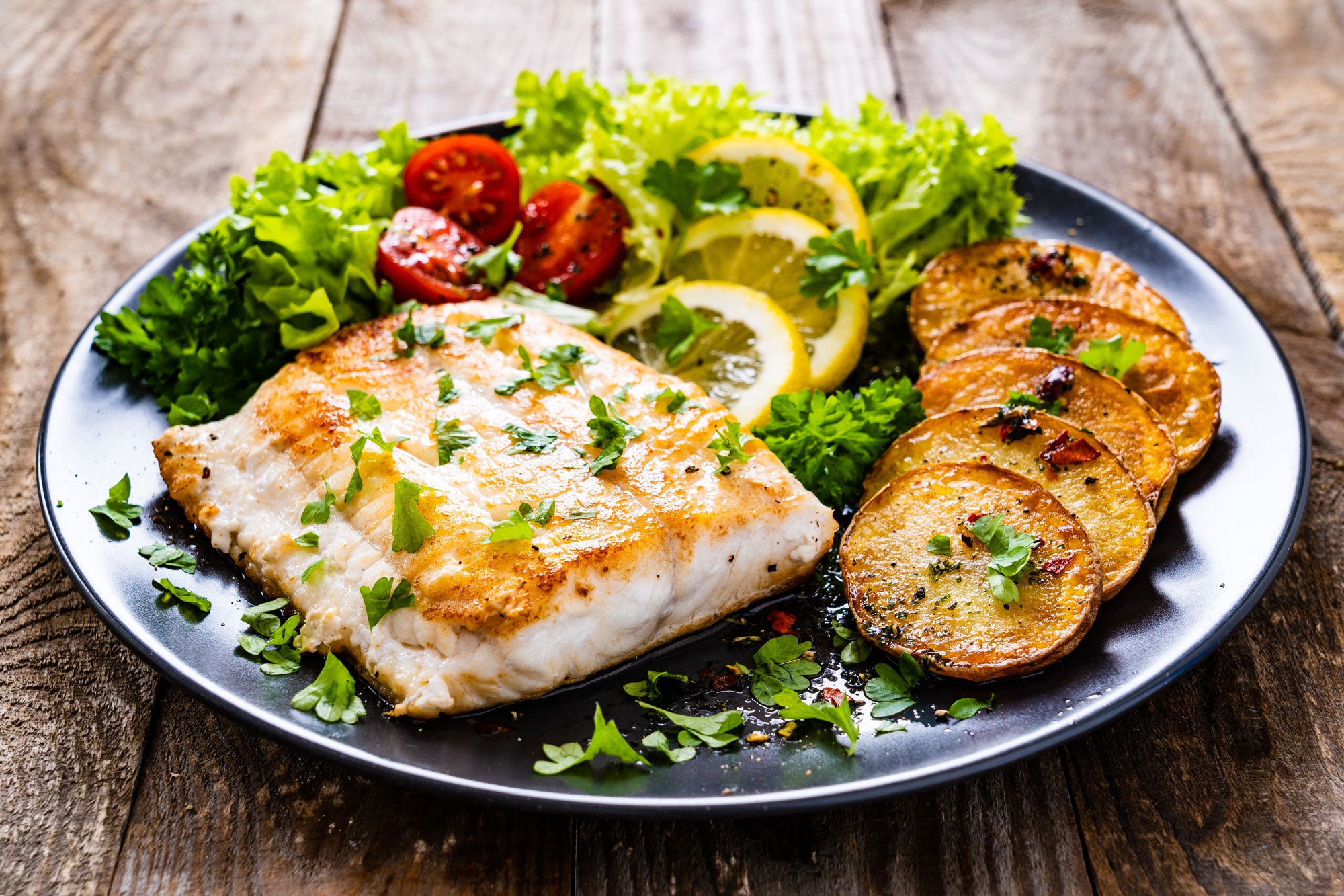 Pacific Cod on a plate with tomatoes, potatoes, lemon and lettuce. Keto-friendly, gluten-free cod recipes. From Fisher to Fork. 