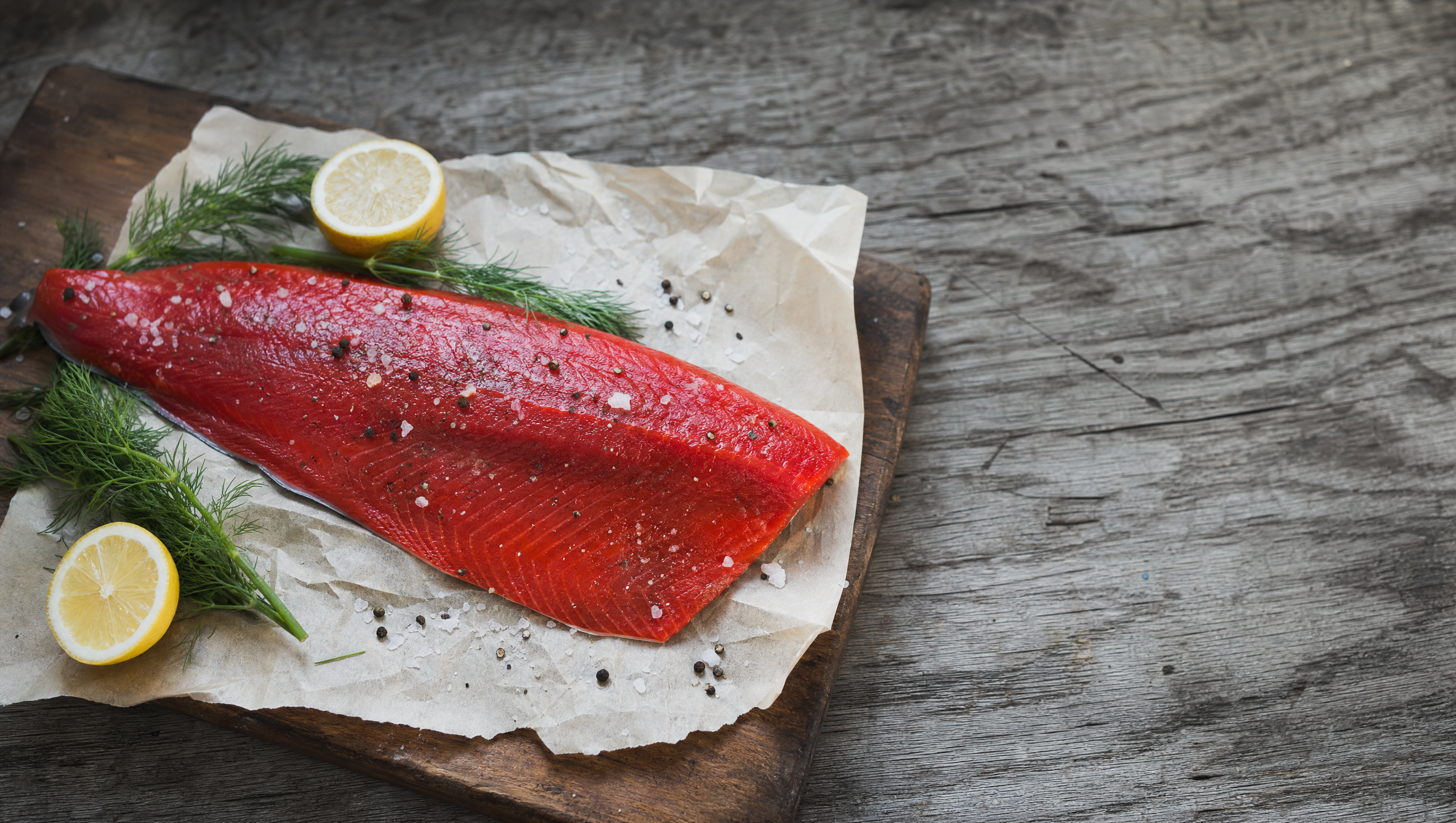Wild Alaskan sockeye salmon fillet on parchment with fresh herbs and lemon